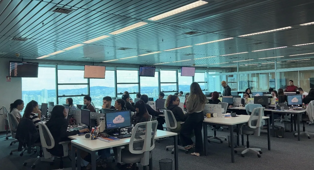 Equipe da OPEN Datacenter no escritório, com painéis de monitoramento e vista para a cidade